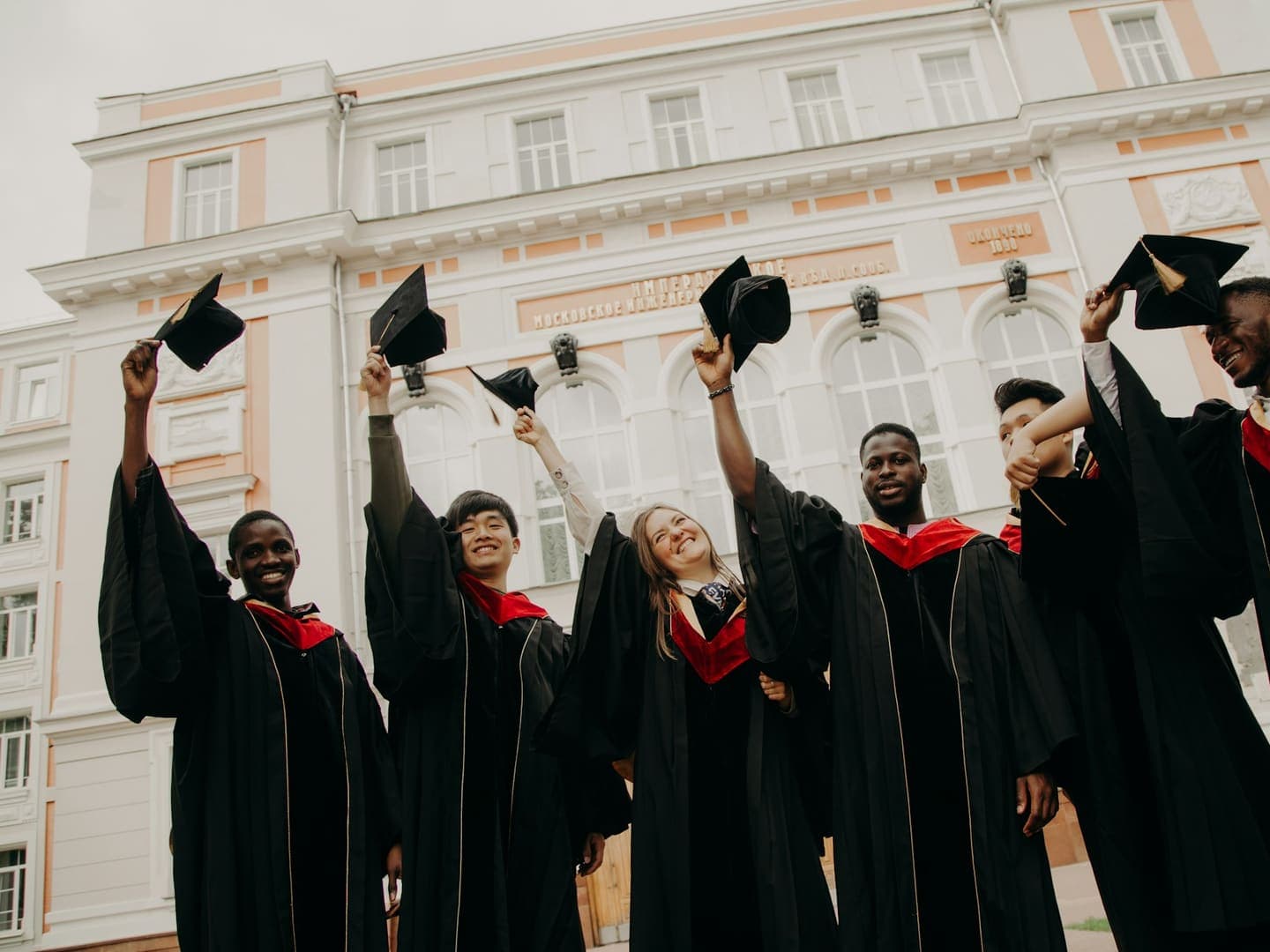 Des diplômés en toge lèvent leur chapeau devant le bâtiment de leur école